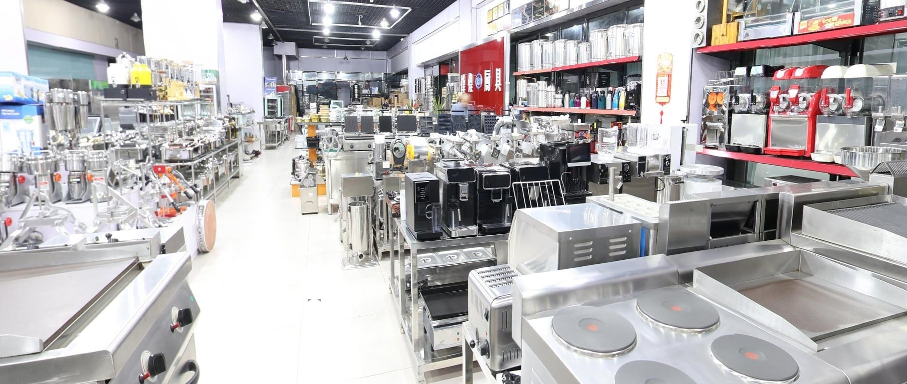 The main aisle of the XFH Kitchen showroom in the Yiwu International Production Materials Market, with the Fenghuang Kitchenware sign on the wall and rows of stainless catering equipment on both sides